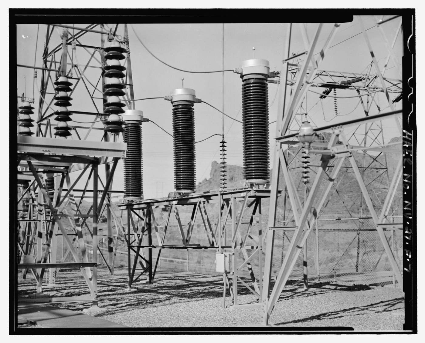 Three tall current transformers with ribbed porcelain insulators in the Hoover Dam switchyard, with steel lattice structures around them.