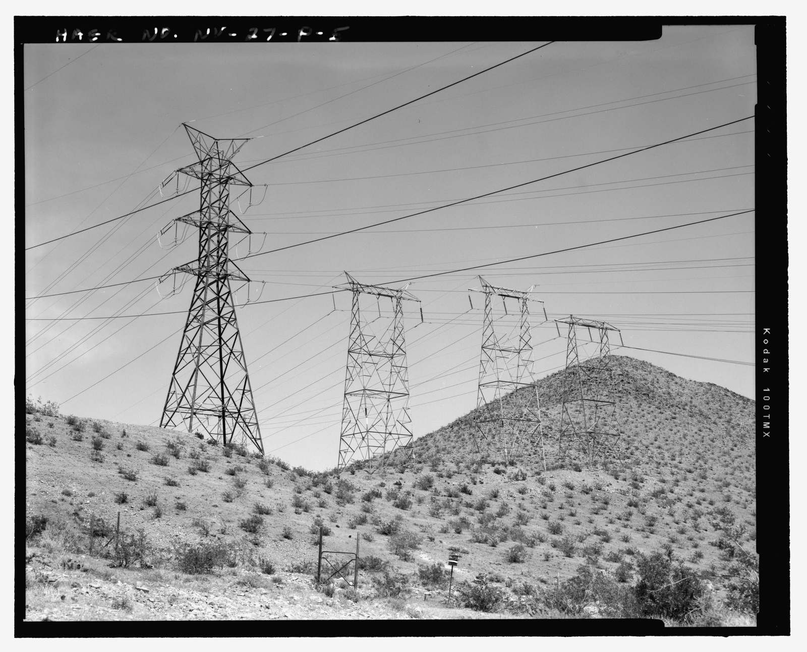 Four steel transmission towers carrying high-voltage lines across desert hills near Hoover Dam.